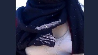 A college girl wearing a hijab reveals her small breasts to her partner in an outdoor setting.